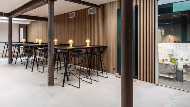 Un interior moderno con una mesa larga y sillas negras, paneles de madera en las paredes y una zona de cocina visible.