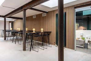 Ein modernes Interieur mit einem langen Tisch und schwarzen Stühlen, Holzwandverkleidungen und einem sichtbaren Küchenbereich.