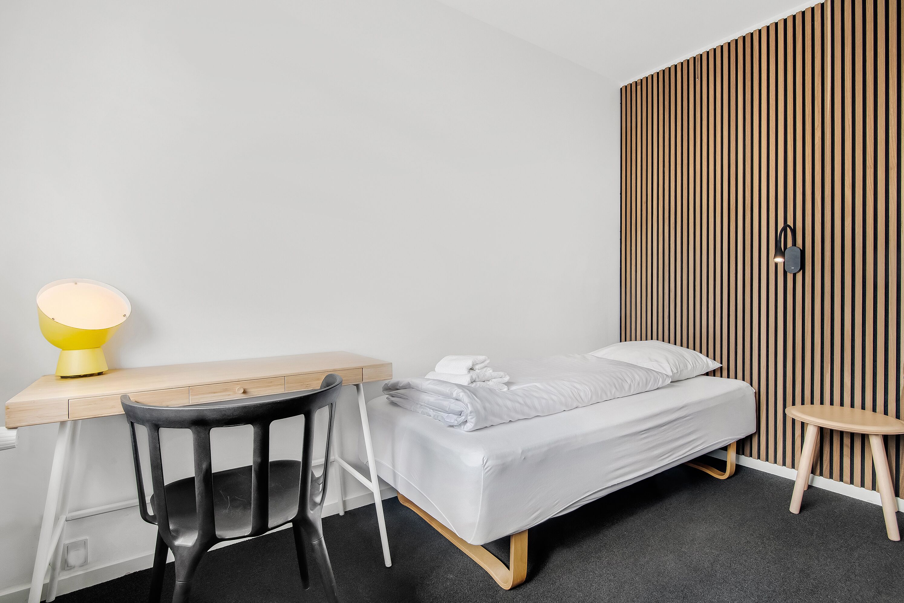 A modern bedroom with a bed, a desk, a chair, and a small table.