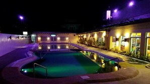 A swimming pool area at night with a building in the background.