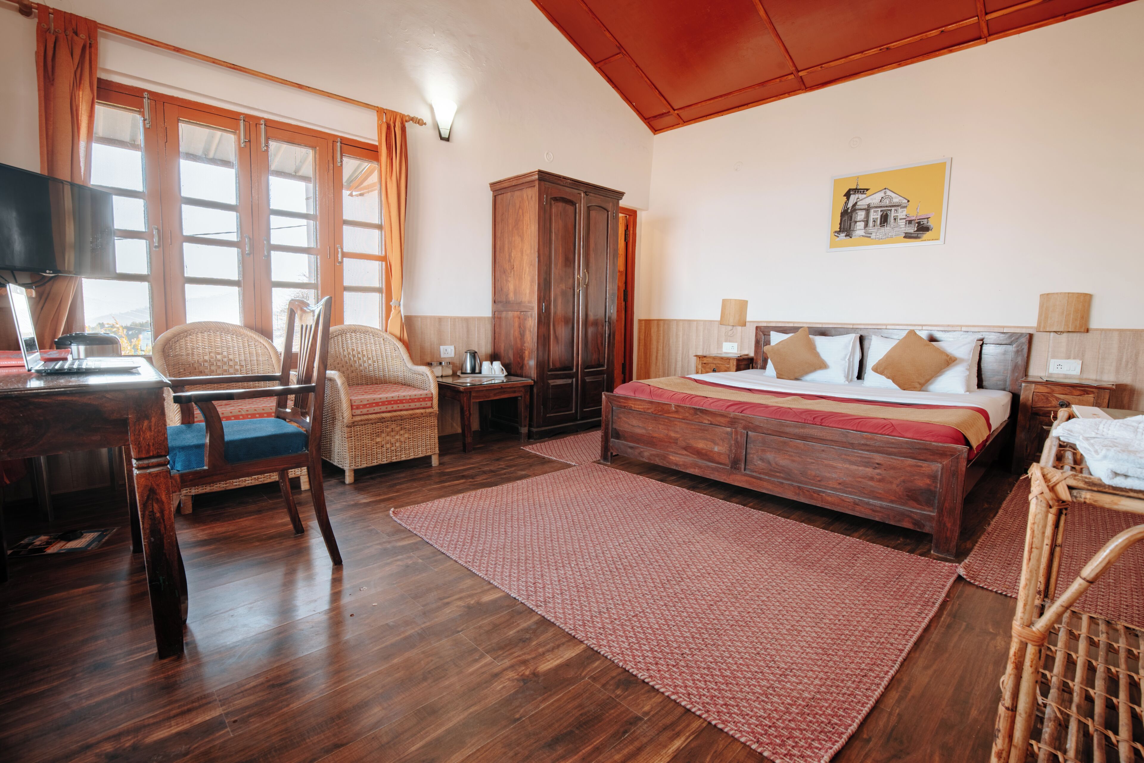 Un dormitorio con cama de madera, dos sillas, un escritorio con una computadora portátil, un armario y una ventana con cortinas.