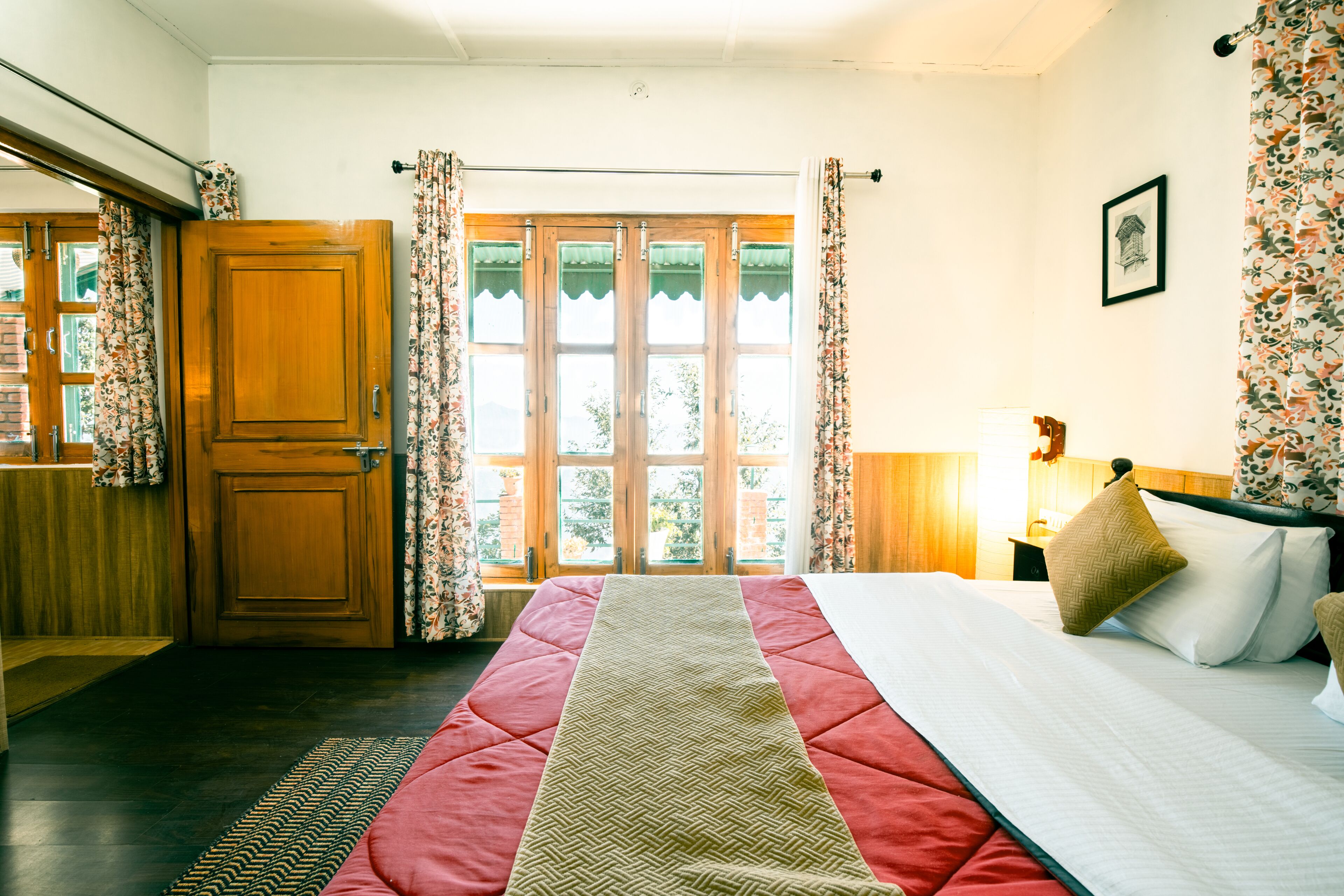 A bedroom with a bed, a wooden wardrobe, a window with curtains, and a framed picture on the wall.