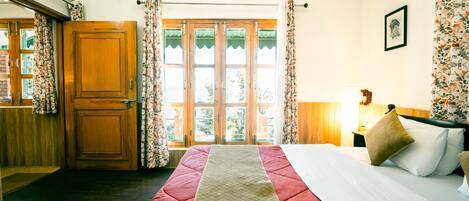 A bedroom with a bed, a wooden wardrobe, a window with curtains, and a framed picture on the wall.
