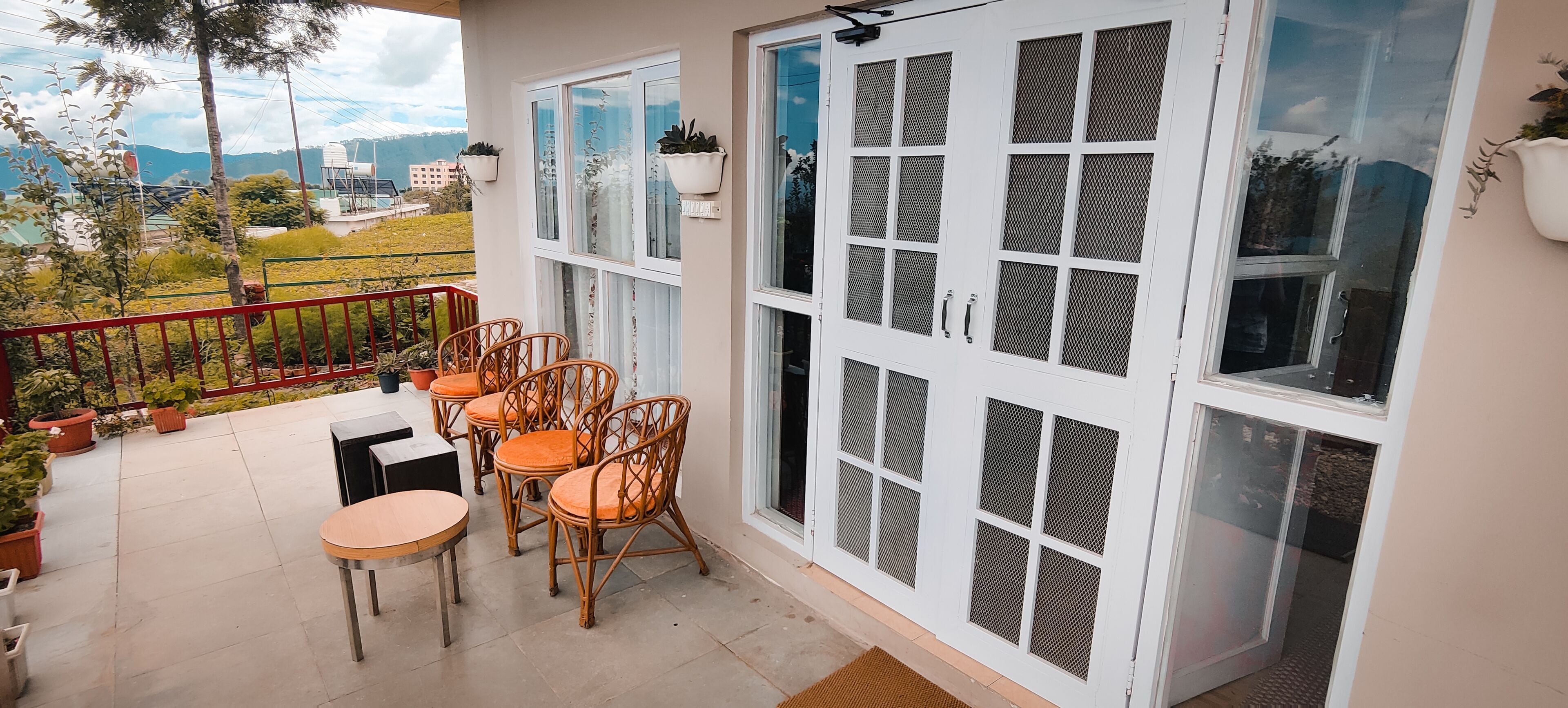 A balcony with wicker chairs and a table, potted plants, and a view of a mountainous landscape.