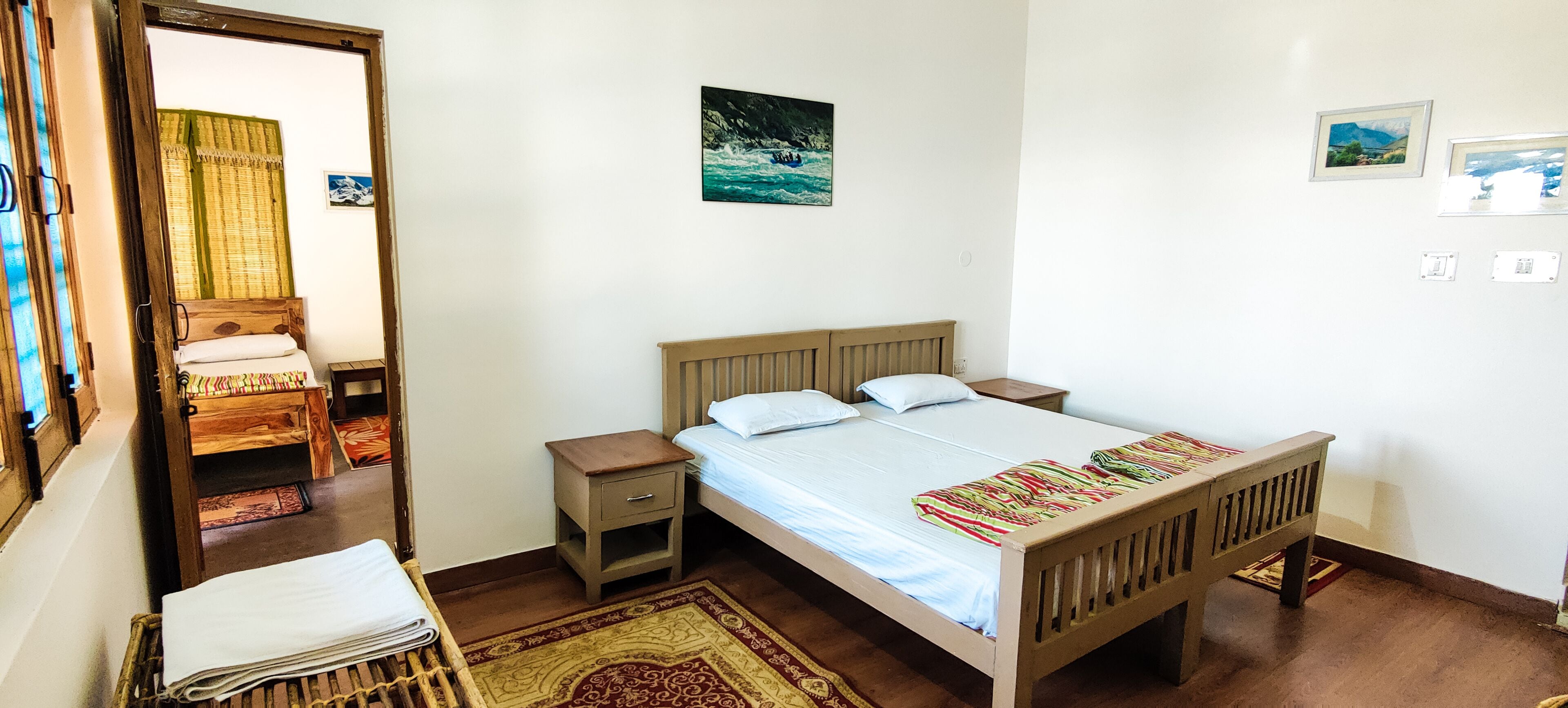 A bedroom with a wooden bed, a nightstand, a small drawer, a mirror, and a window with curtains.