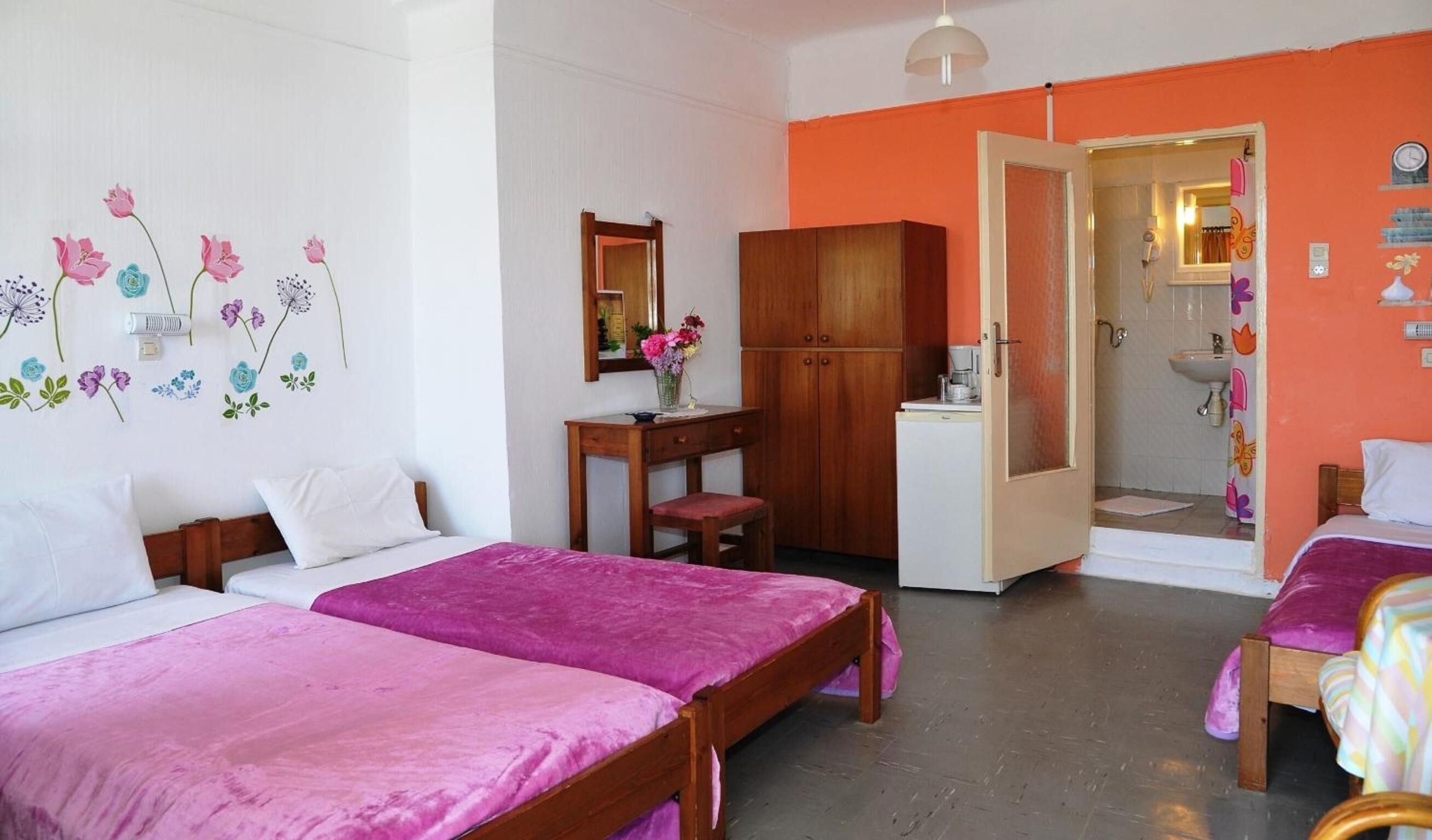 Ein Zimmer mit zwei Betten, einem Holztisch, einem Kleiderschrank und einem durch eine geöffnete Tür einsehbaren Badezimmer.