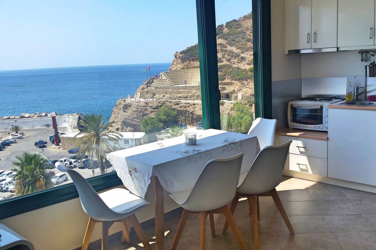 A balcony with a table and chairs overlooking a coastal view.