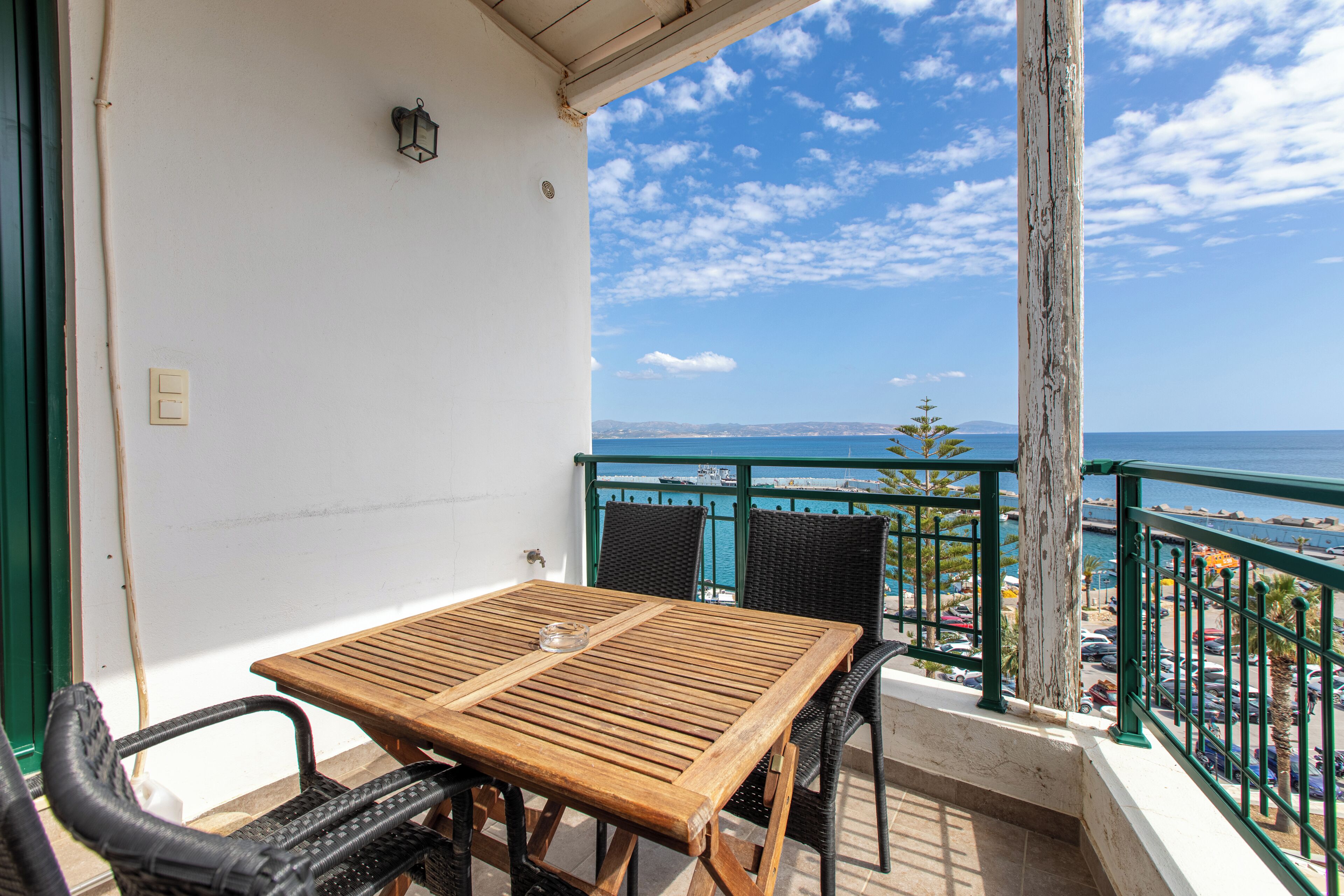 A balcony with a wooden table and chairs, a view of the sea, and a railing.