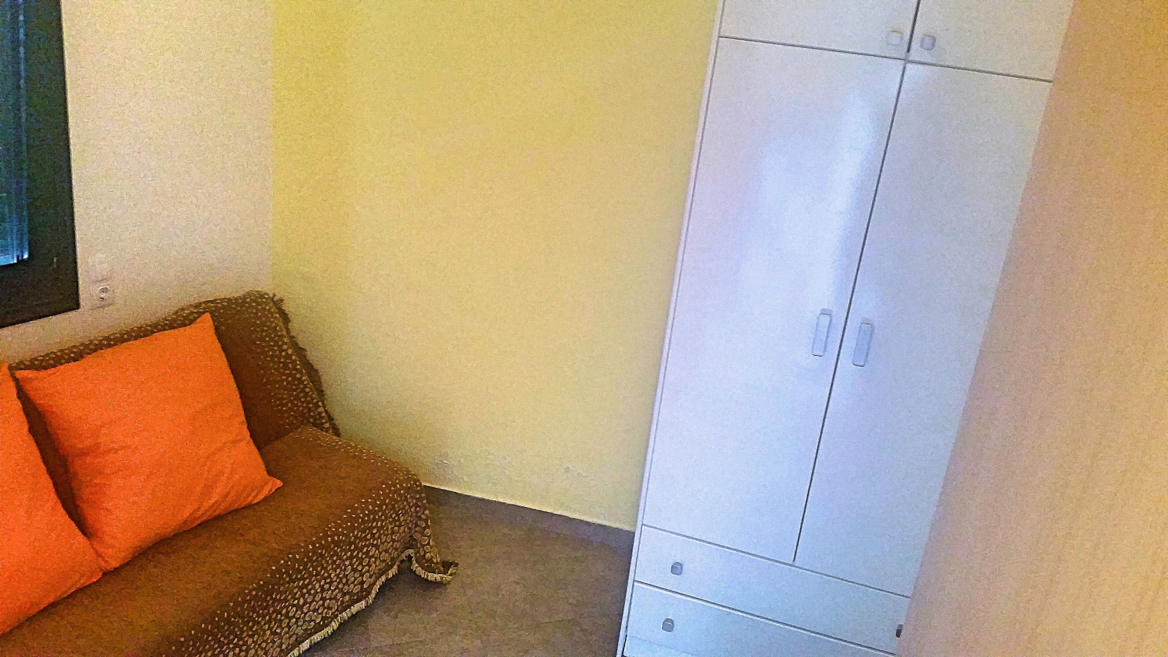 Una habitación con un sofá marrón, un cojín naranja y un armario blanco.