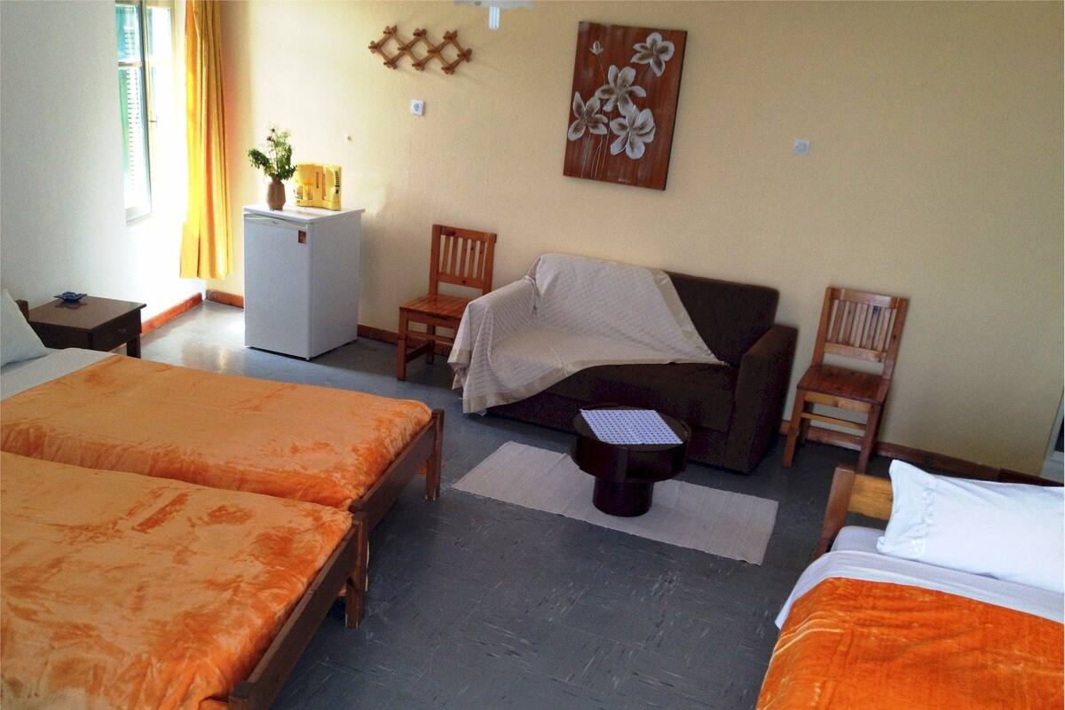 A hotel room with two beds, a sofa, a small table, a refrigerator, and a wall-mounted artwork.