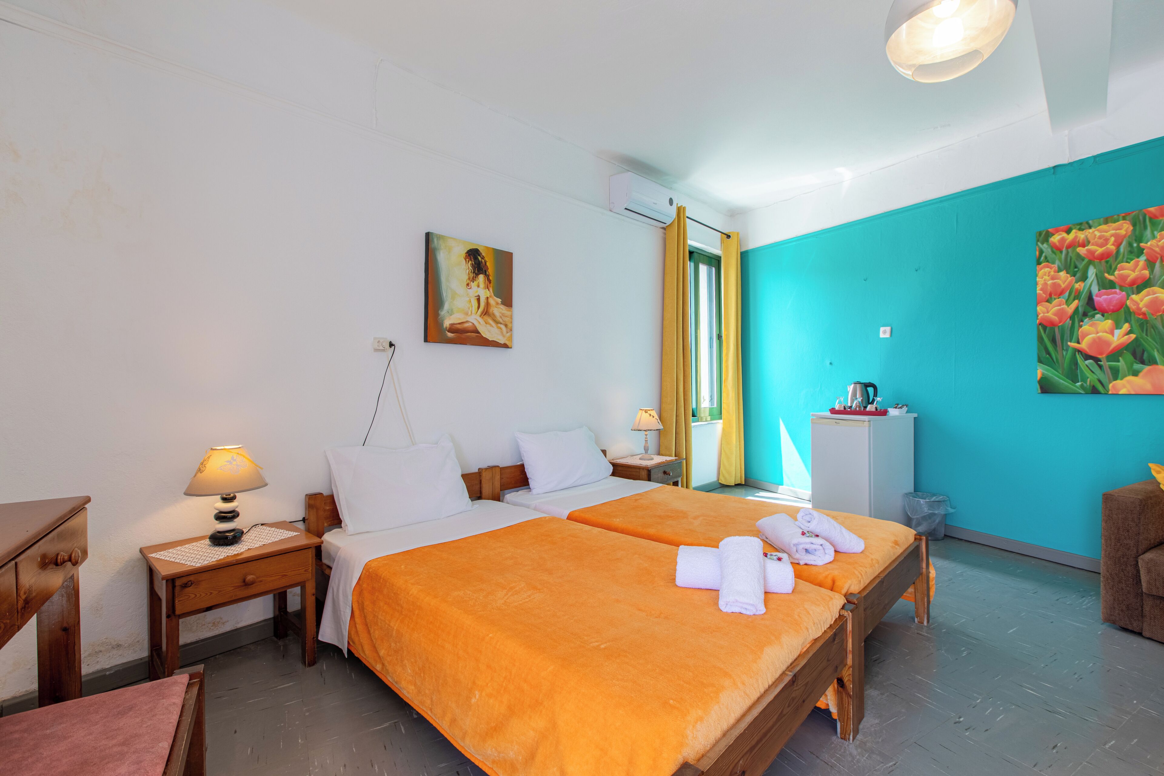 A hotel room with two beds, a desk, a chair, a lamp, a painting, and a window with curtains.