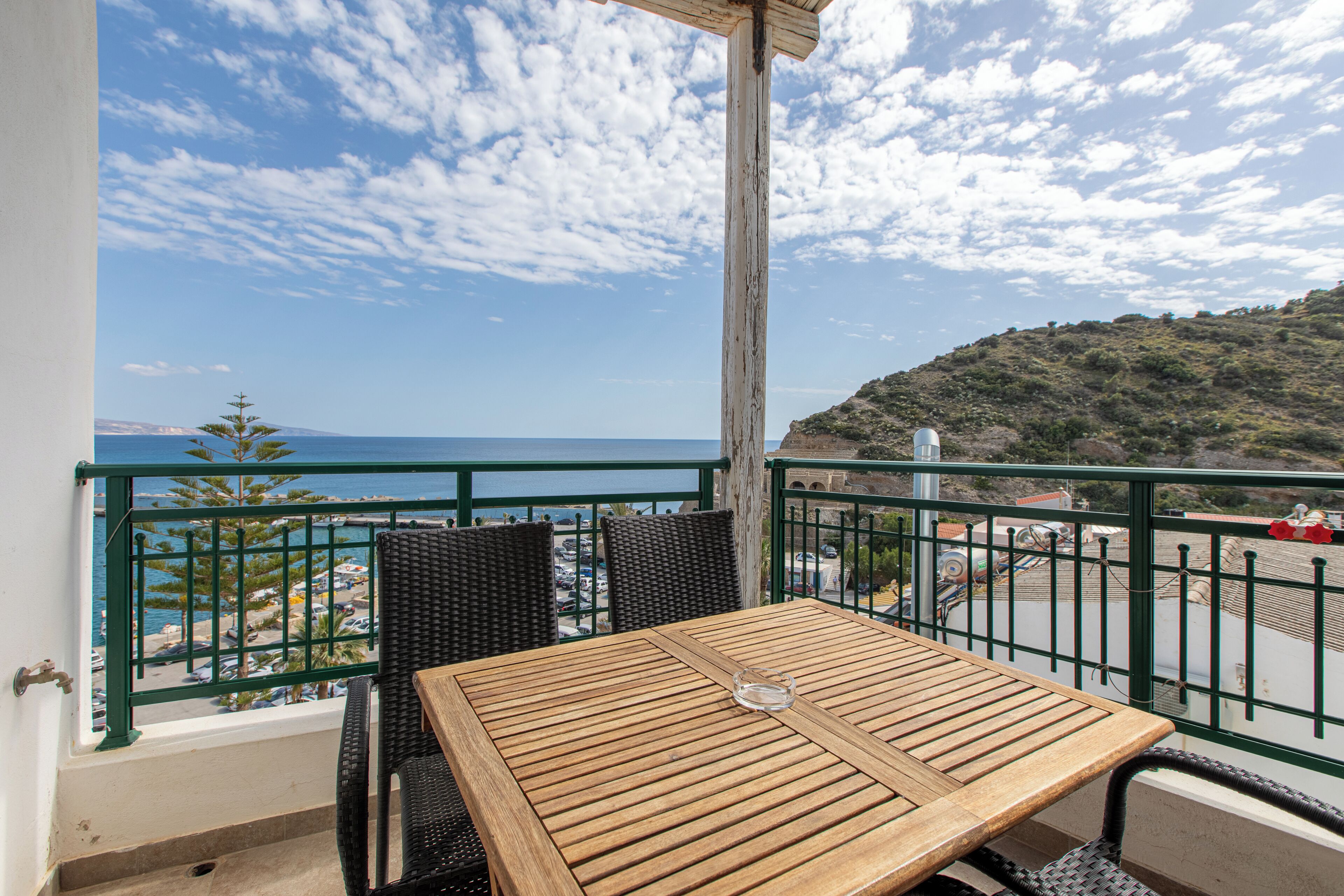 Un balcón con una mesa y sillas de madera, con vistas a la costa y un cielo despejado.