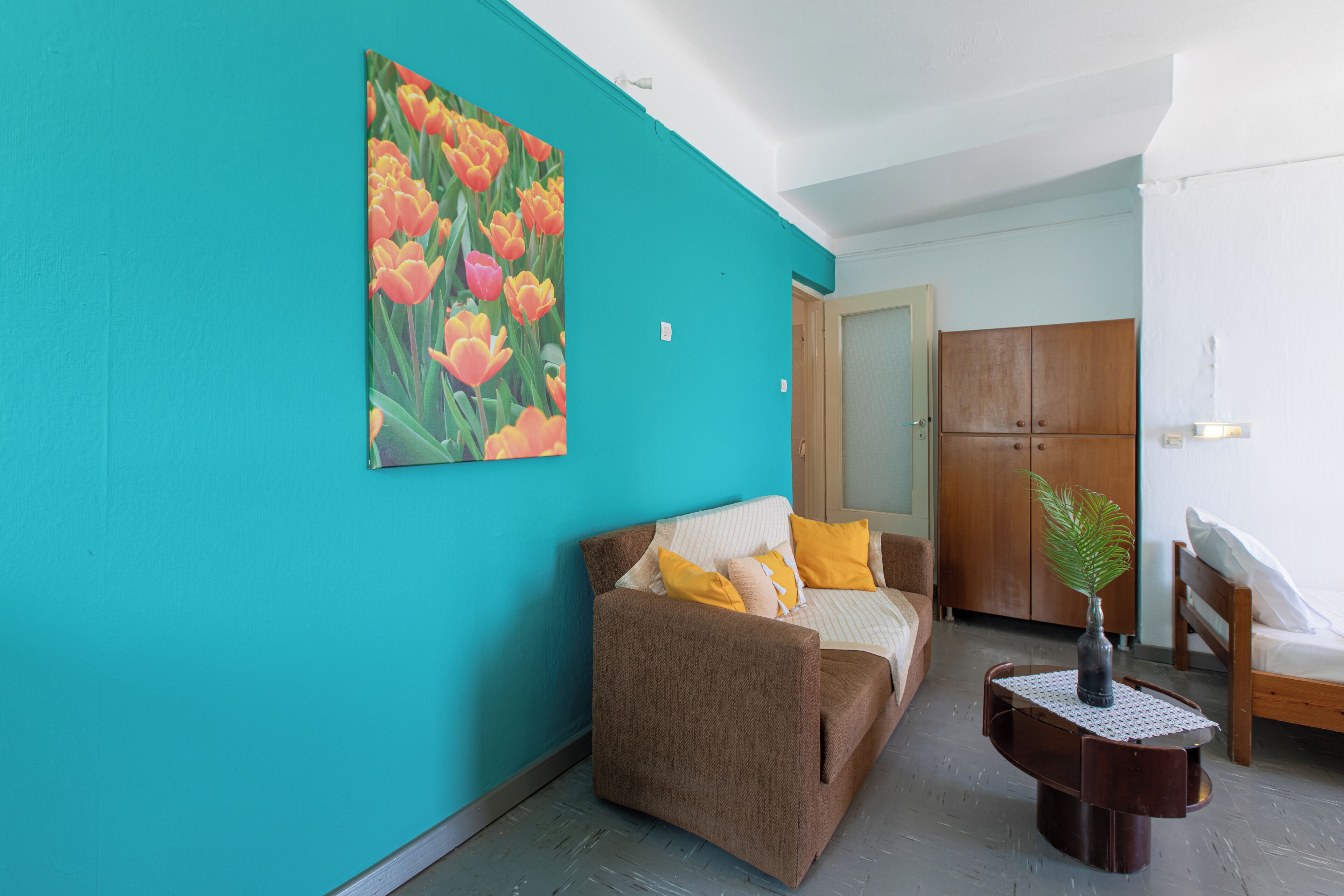 Ein Zimmer mit türkisfarbenen Wänden, einem braunen Sofa mit gelben Kissen, einem Holzschrank und einem kleinen Tisch mit einer Vase.