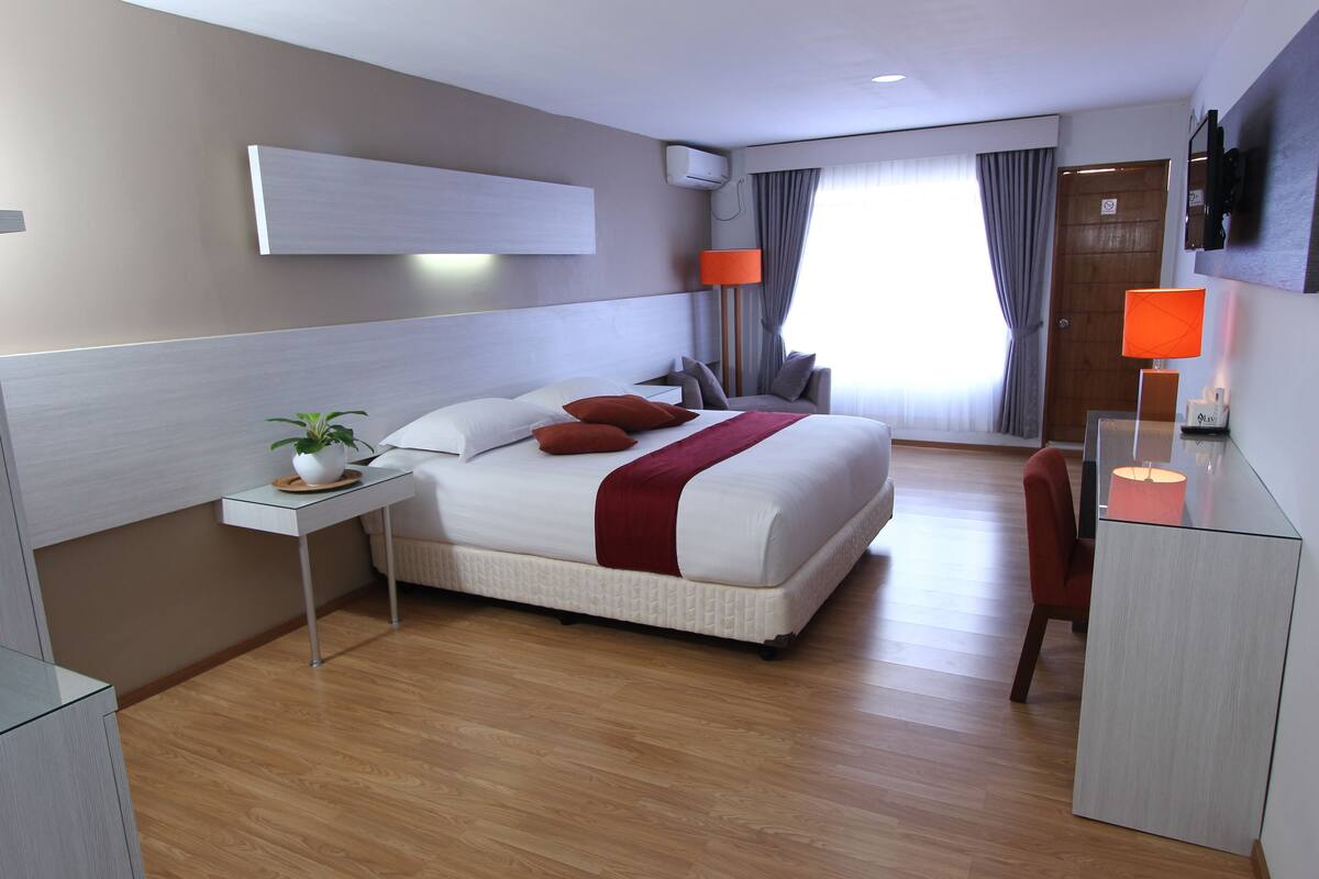A modern hotel room with a large bed, a desk, a chair, a TV, and a window with curtains.