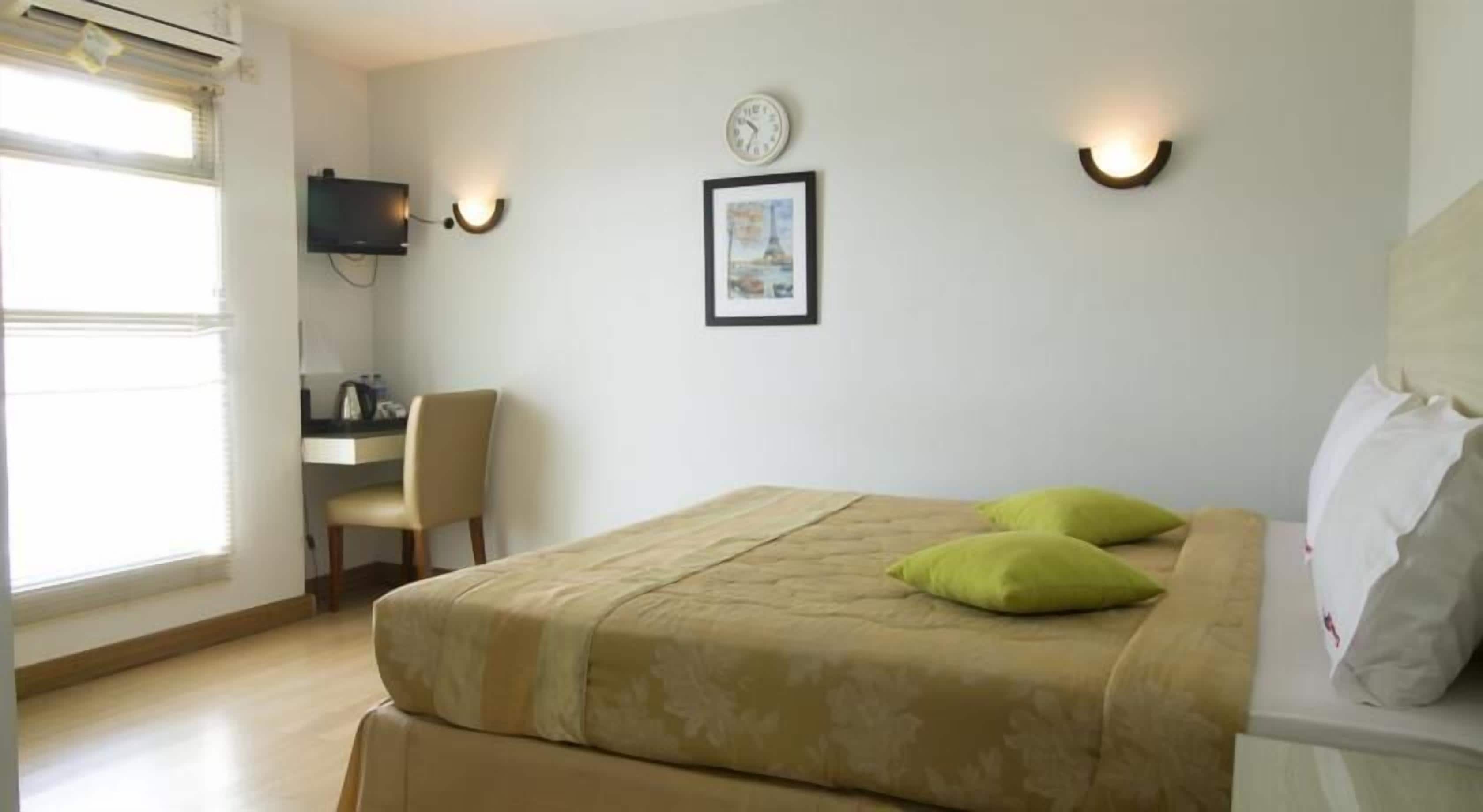 A hotel room with a bed, a desk, a chair, and a wall-mounted clock.