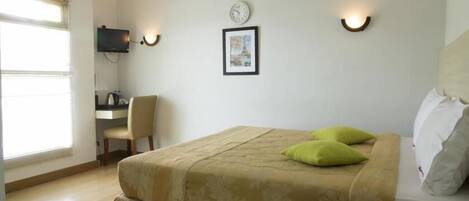A hotel room with a bed, a desk, a chair, and a wall-mounted clock.