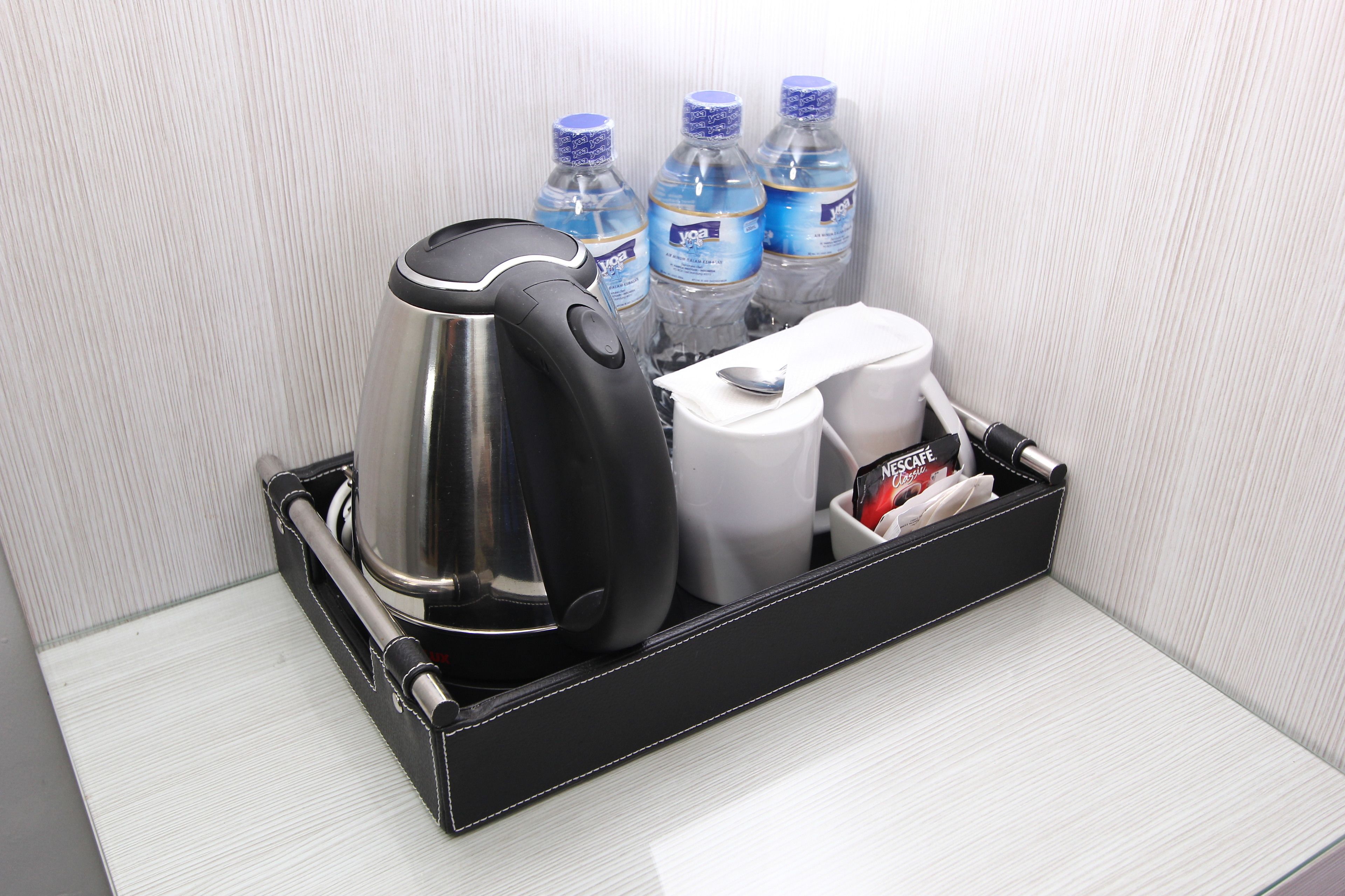 A black tray with a kettle, two bottles of water, a coffee maker, and a container of tea bags.