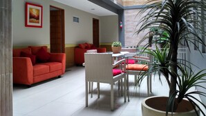 Un espacio interior amplio con un sofá rojo, un sillón de mimbre blanco y una mesa con una planta en maceta.