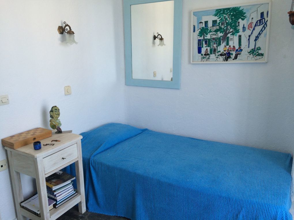 A room with a bed, a small bedside table with books, a mirror, and a wall painting.