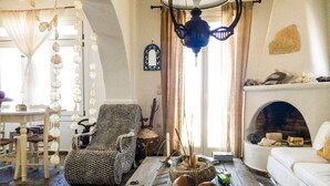 A cozy living room with a fireplace, a woven armchair, and a rustic wooden floor. - Kanalia Villas (Mykonos)