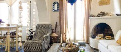 Una sala acogedora con chimenea, un sillón de fibras naturales y un suelo de madera rústica.