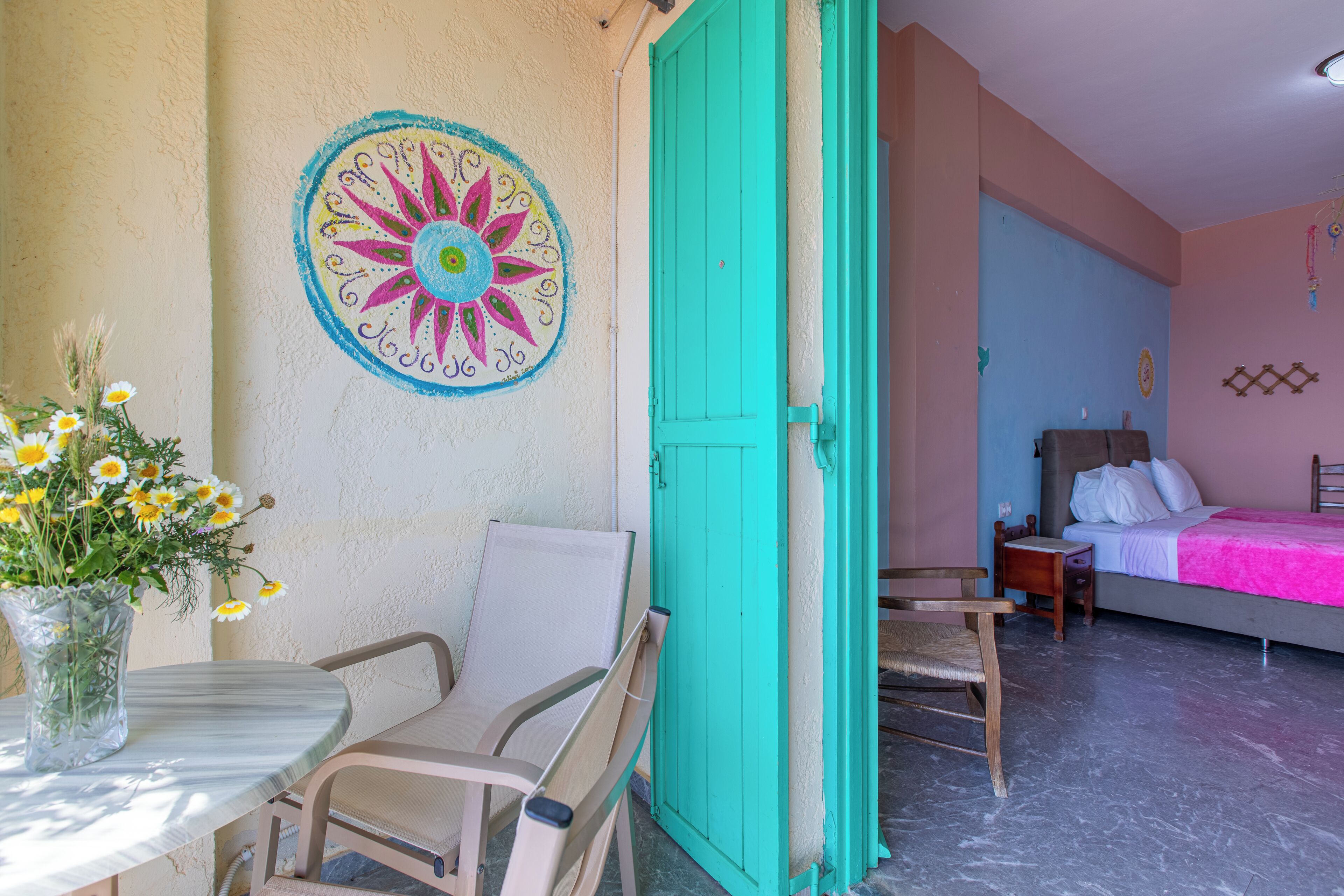 Una habitación con una cama, una silla, una mesa con un florero y una pared con un diseño circular.