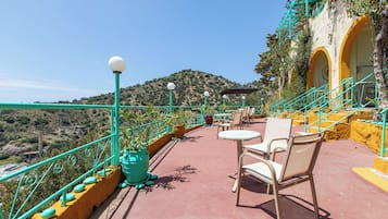 Una terraza con sillas y mesas, barandilla y vistas a un paisaje montañoso.