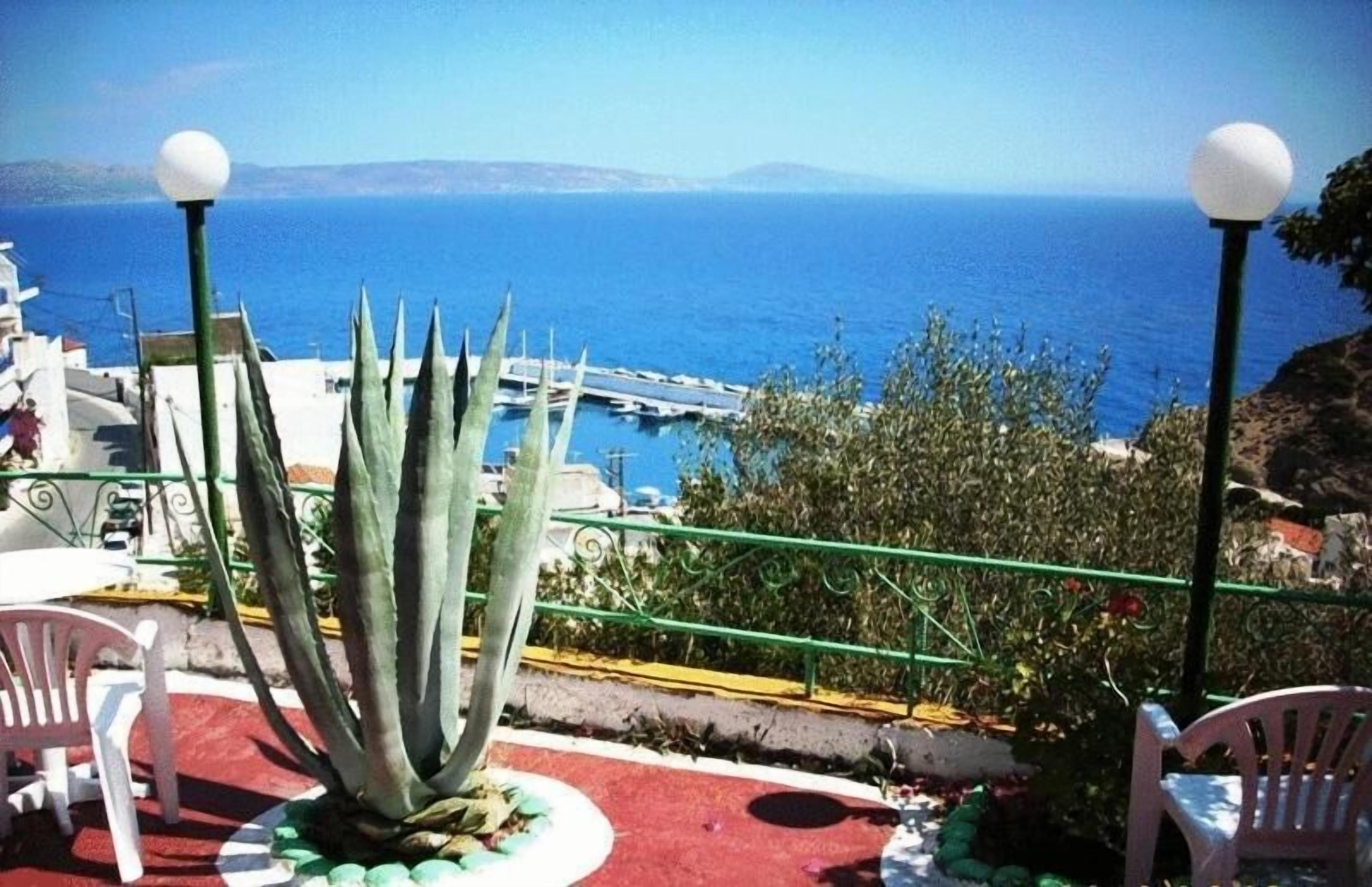 Terraza con vistas al mar, que incluye una planta de agave grande, dos sillas blancas y una barandilla.