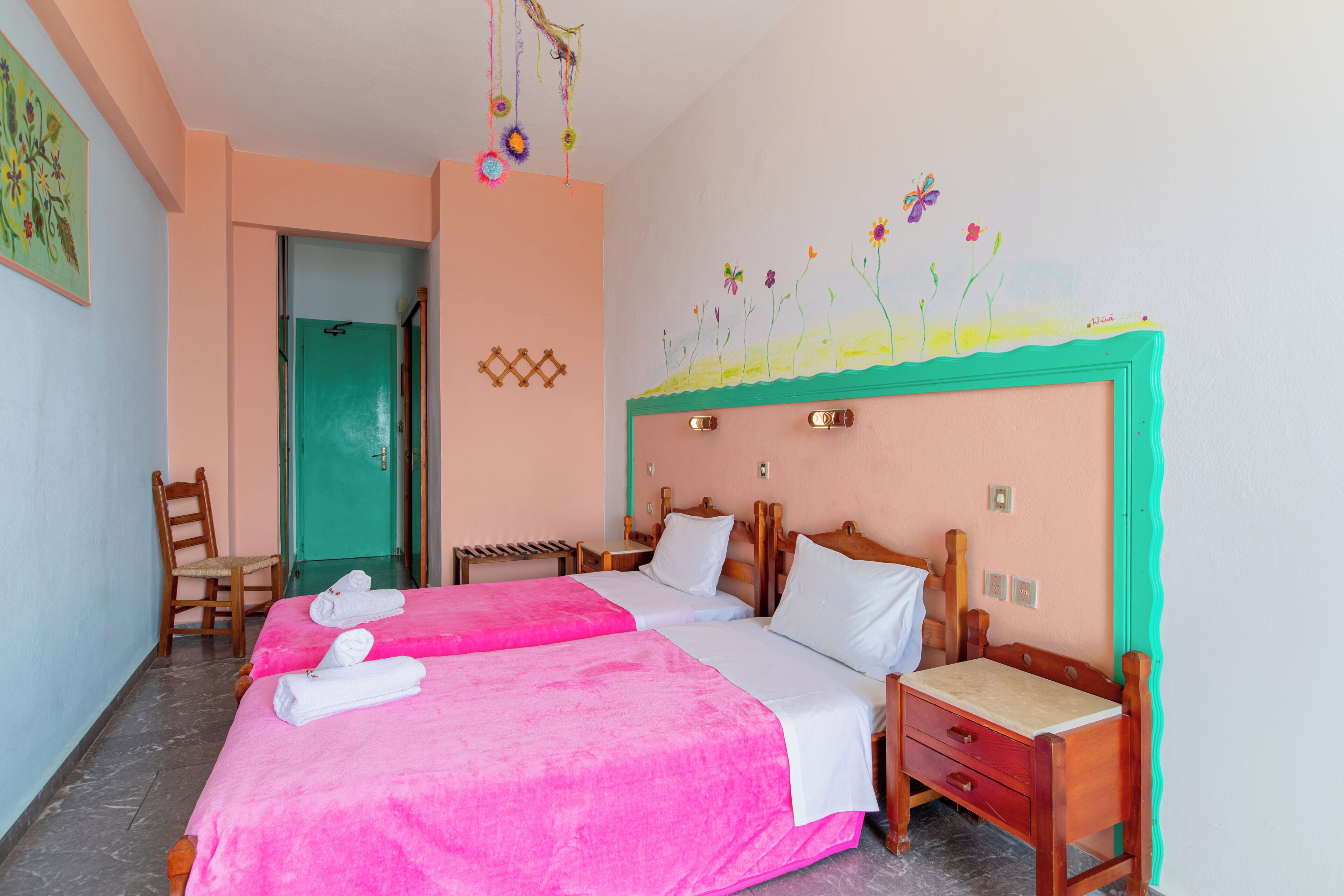 A hotel room with two beds, a wooden nightstand, a chair, and a door leading to another room.