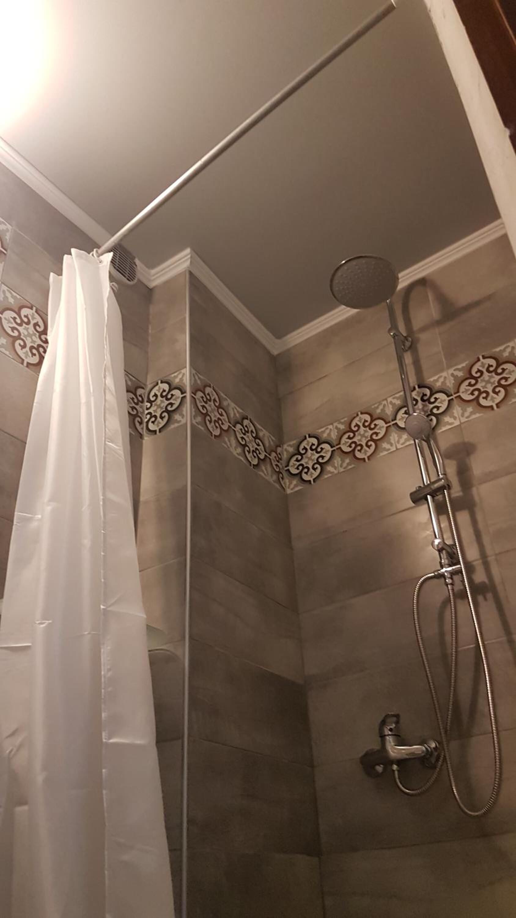 Un espacio de ducha con cabezal, ducha de mano y cortina.