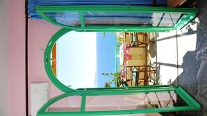 A room with a large window overlooking a beach, a bed, and a chair. - Erofili Rooms (Agios Vasileios)