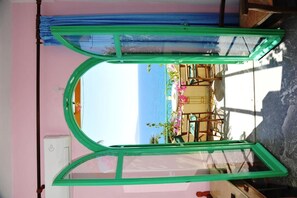A room with a large window overlooking a beach, a bed, and a chair. - Erofili Rooms (Agios Vasileios)