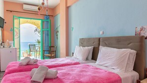 A double bed with pink and white bedding, a wooden headboard, and a view of the sea through an open door. - Erofili Rooms (Agios Vasileios)