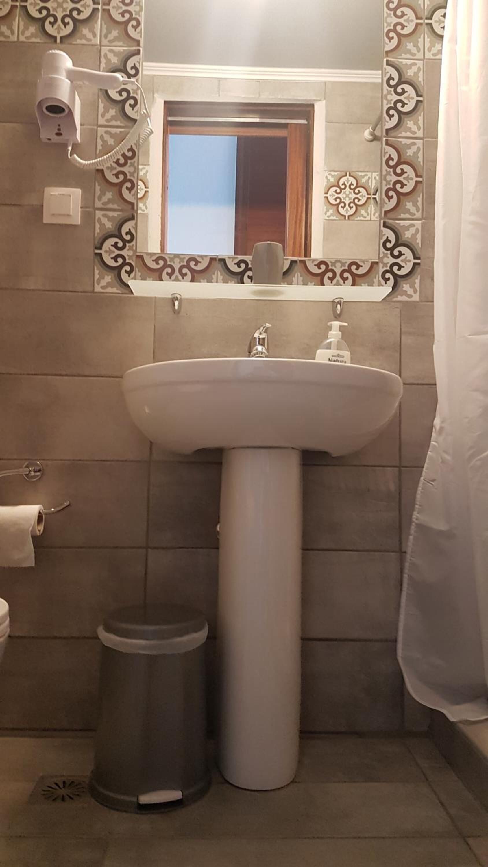 Une salle de bain équipée d’un lavabo sur colonne, d’un sèche-mains, d’une poubelle et d’un miroir avec un cadre décoratif.