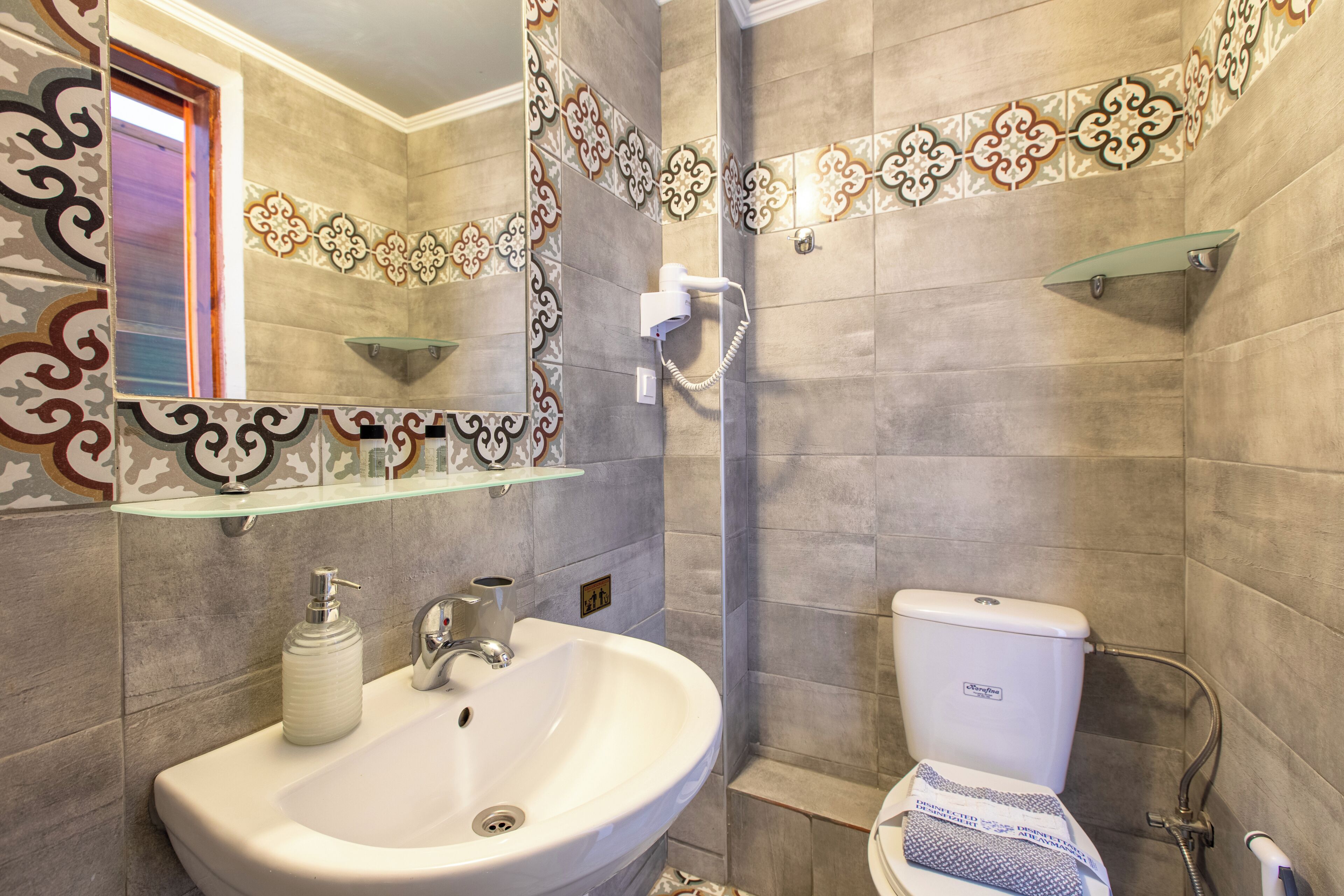 A bathroom with a sink, mirror, toilet, shower, and decorative tiles.