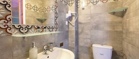 A bathroom with a sink, mirror, toilet, shower, and decorative tiles.
