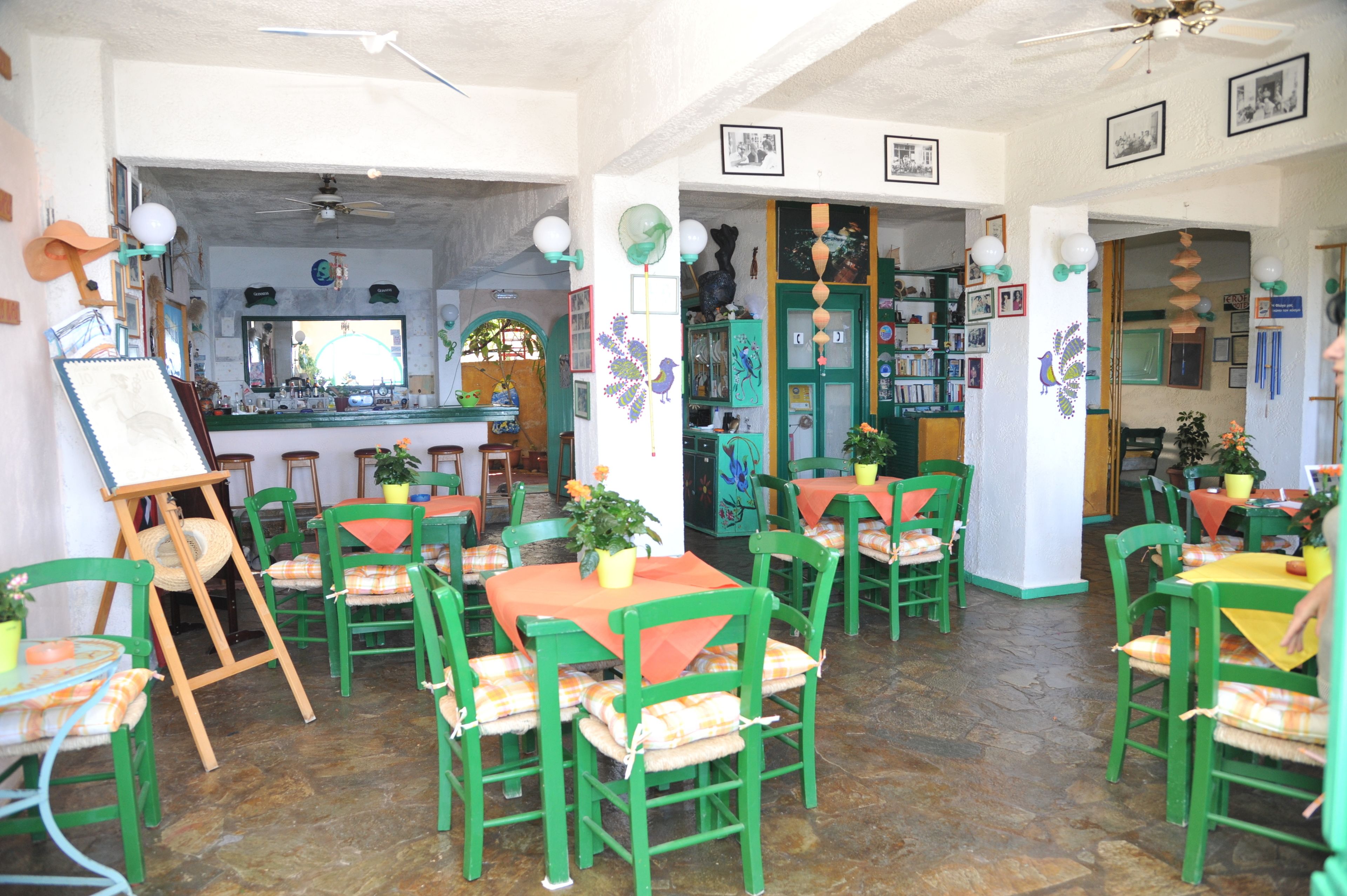 A dining area with green chairs and orange tablecloths, a bar area with a counter, and various decorations on the walls.