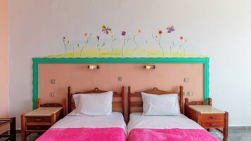 A room with two beds, a green-framed headboard, and a wall mural with flowers and butterflies.
