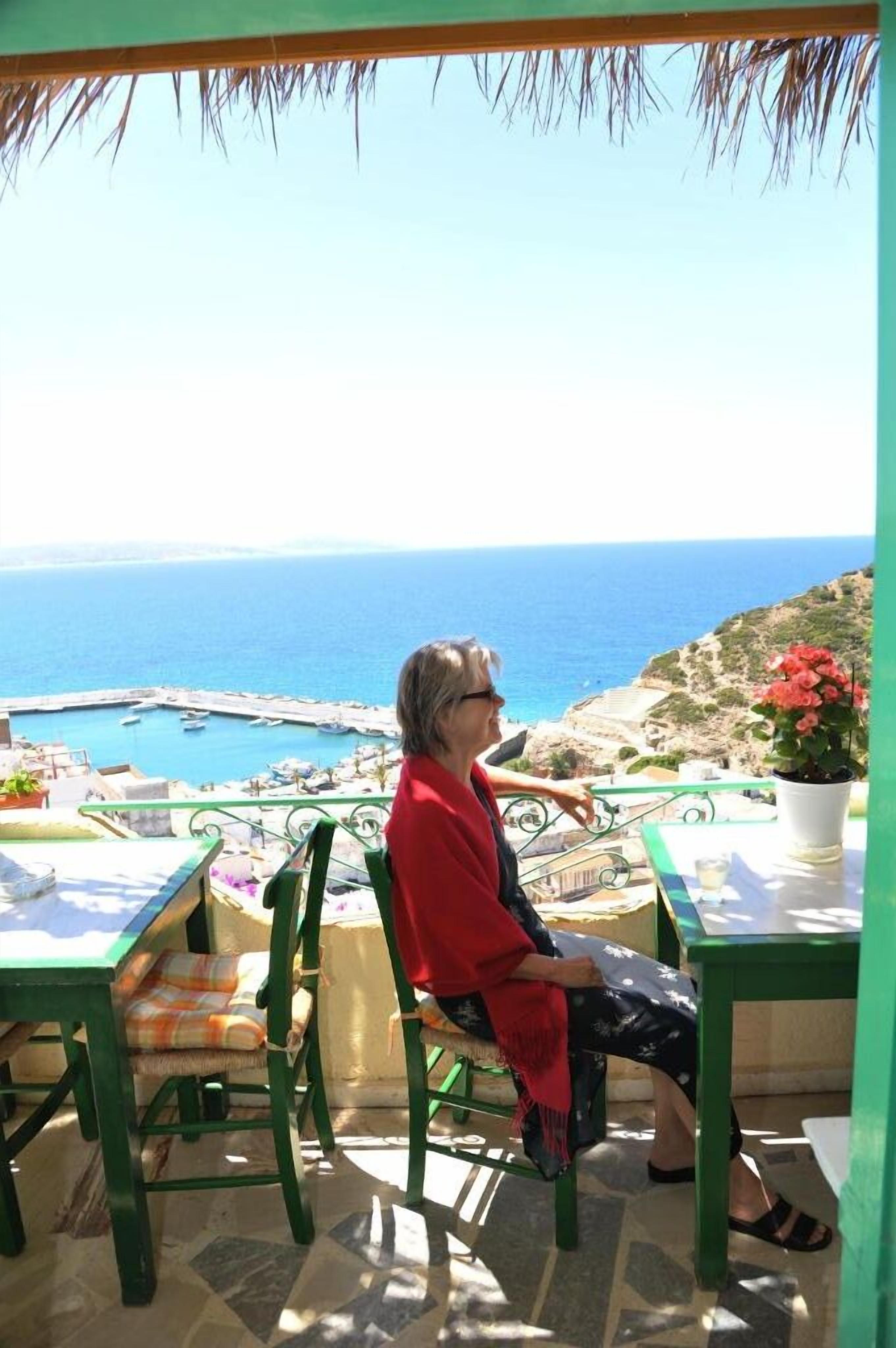 Une personne assise à une table, avec vue sur la mer et les bateaux.