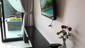Una habitación moderna con una televisión de pantalla plana montada en la pared, un comedor con una mesa negra, dos tazas blancas y un jarrón con rosas rojas.