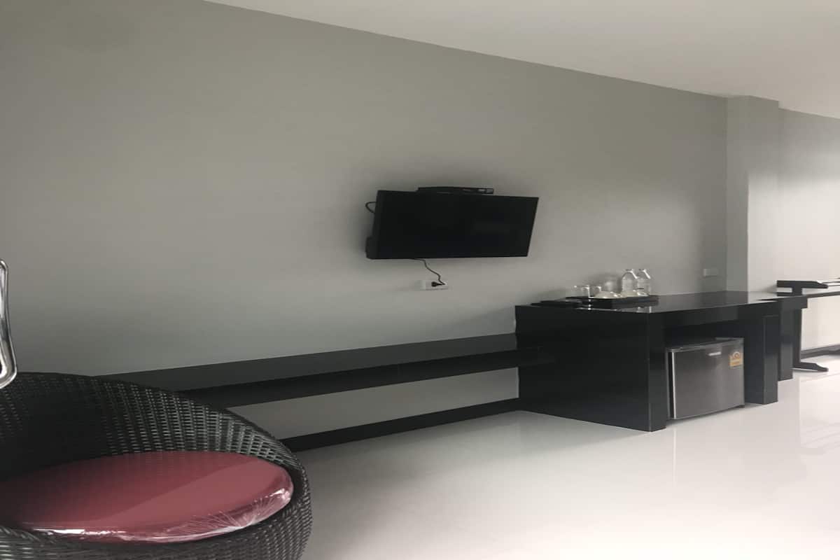 A modern hotel room with a flat-screen TV mounted on the wall, a black minibar, and a wicker chair with a red cushion.
