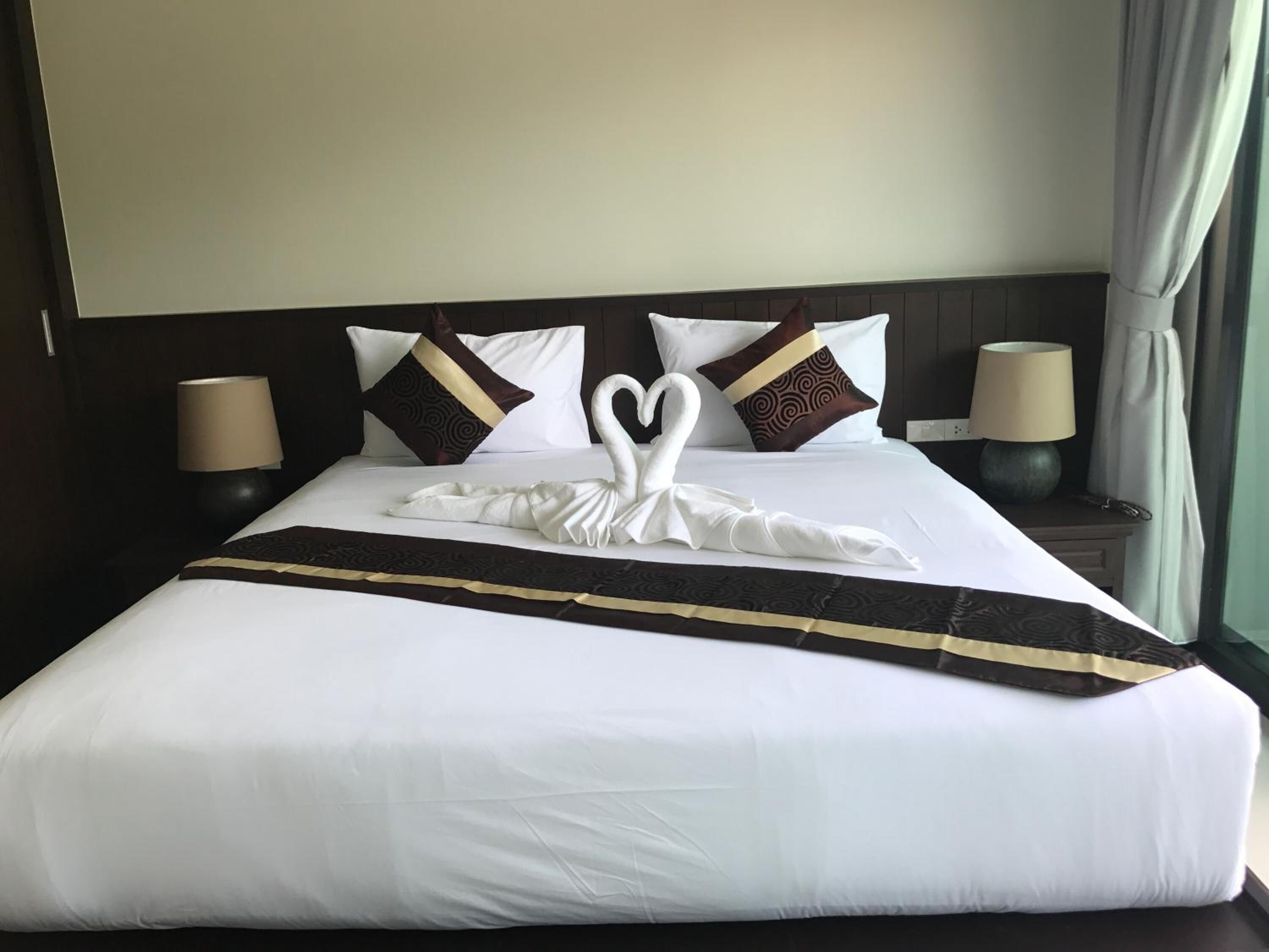 A hotel room with a neatly made bed, two bedside lamps, and a window with curtains.