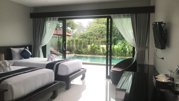 Habitación de hotel con dos camas, televisor, mesa de comedor y vista a una piscina y zonas verdes.