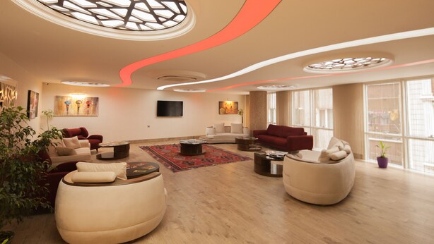 A spacious living room with modern furniture, a large window, and a unique ceiling design. - Armin Hotel (Amasya)