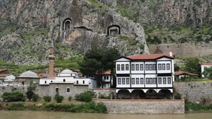A historic building with a white facade and black trim, located near a river and rocky cliffs. - Armin Hotel (Amasya)