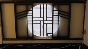 A window with a grid design and a circular center, allowing light to pass through. - Taito Ryokan (Tokyo)