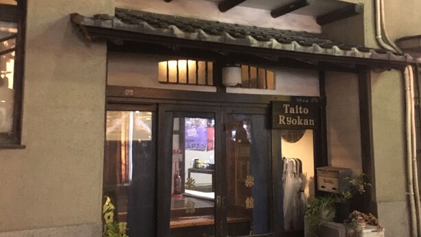A building with a traditional facade, a sign reading "Taito Ryokan," and potted plants at the entrance. - Taito Ryokan (Tokyo)