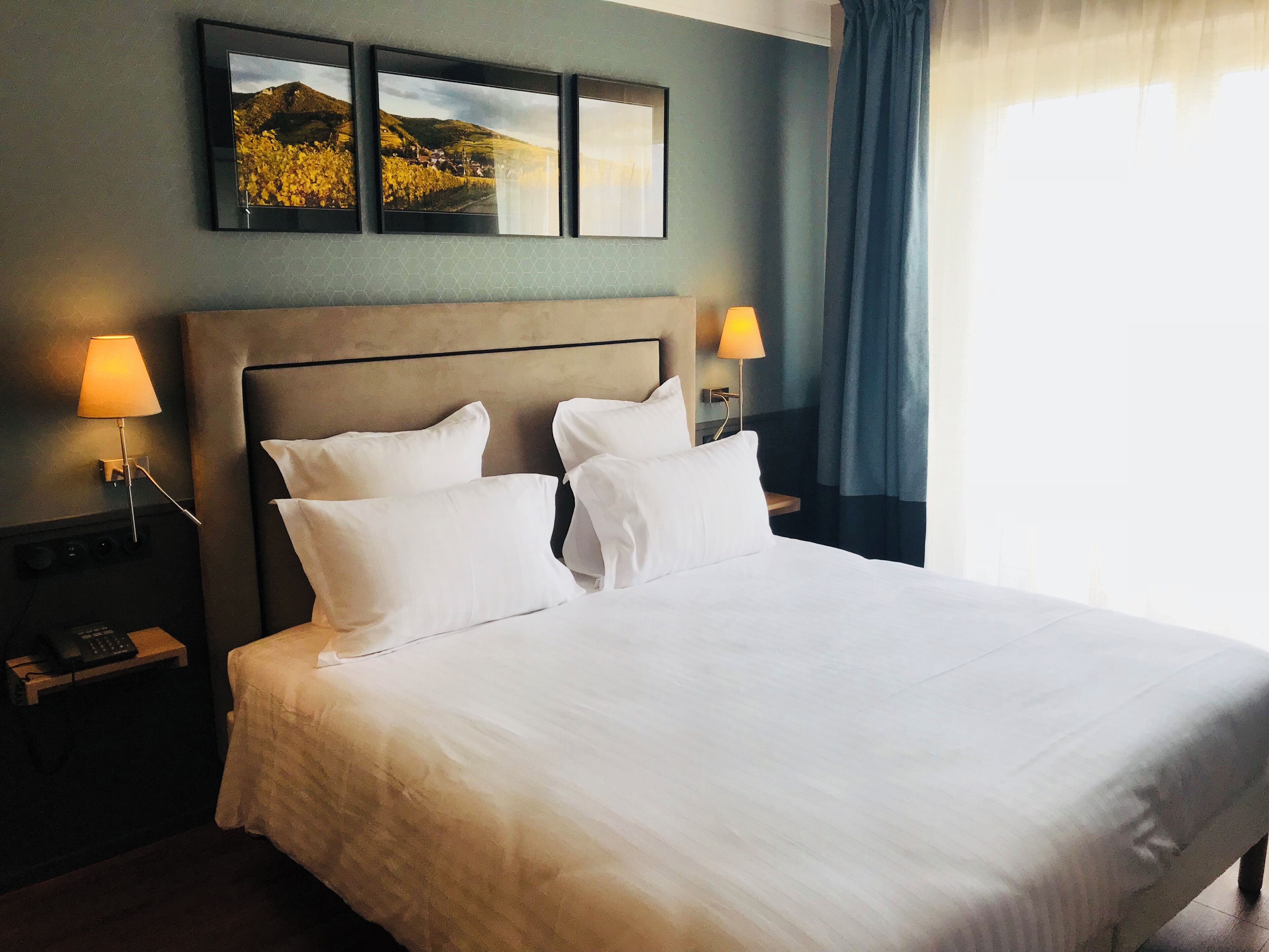 Ett hotellrum med en stor säng, två sänglampor, ett nattduksbord med en telefon och tre inramade tavlor på väggen.