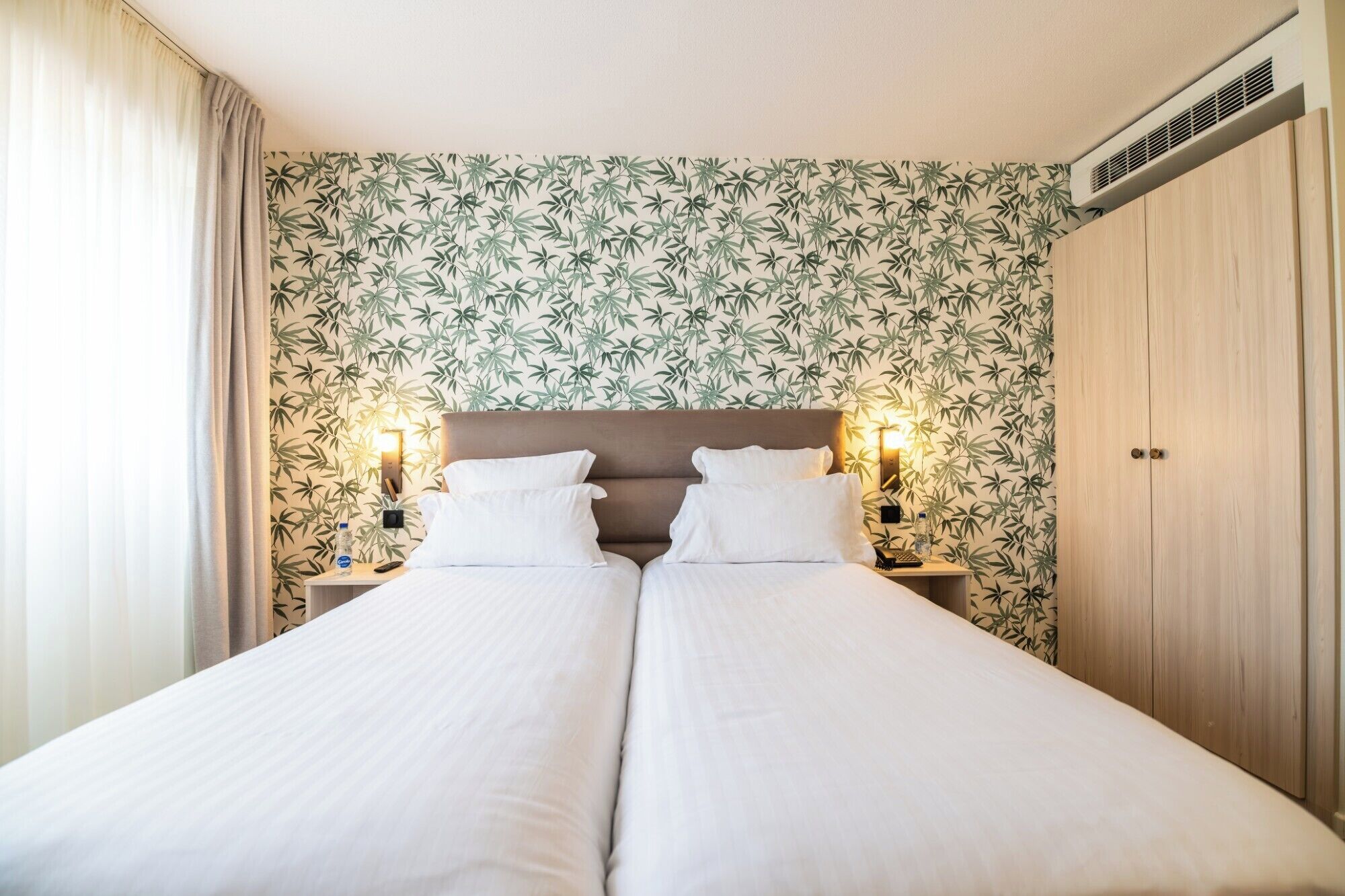 Un lit double avec deux tables de chevet, une tête de lit et un mur orné d’un motif de feuilles de bambou.