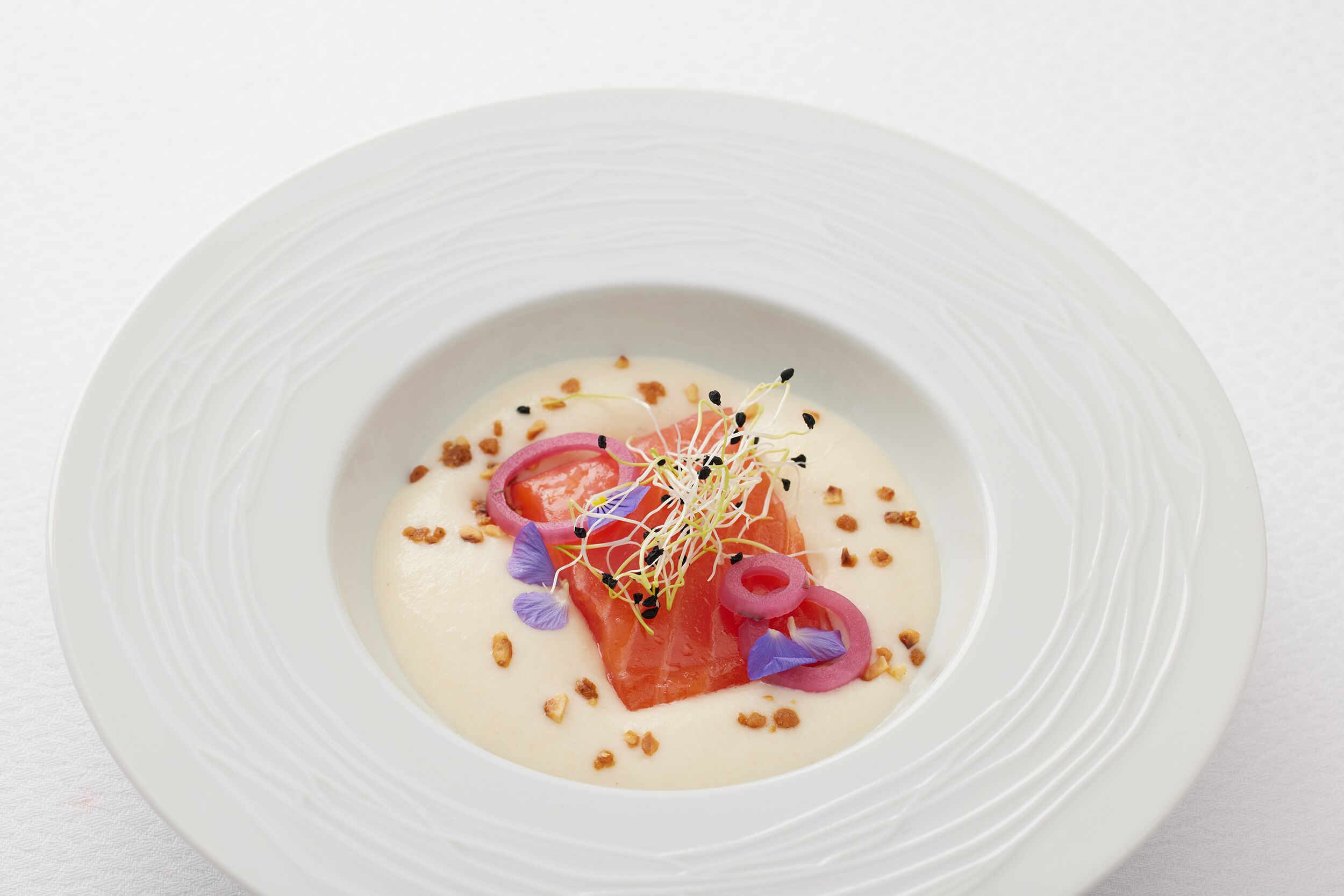 A white plate with a salmon dish, garnished with purple flowers and edible flowers.